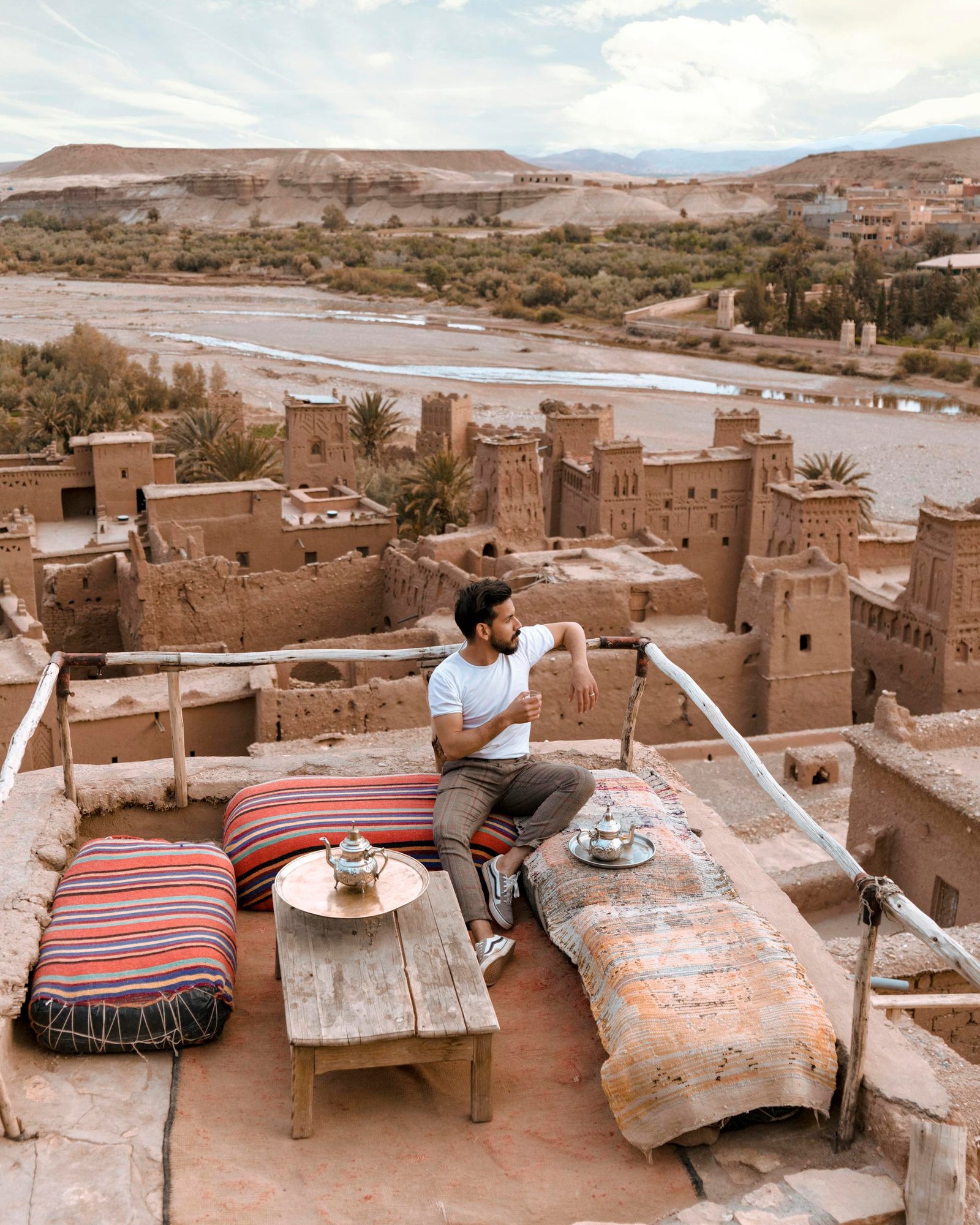 Man enjoying tea on a rooftop terrace overlooking Ait Benhaddou, Morocco.