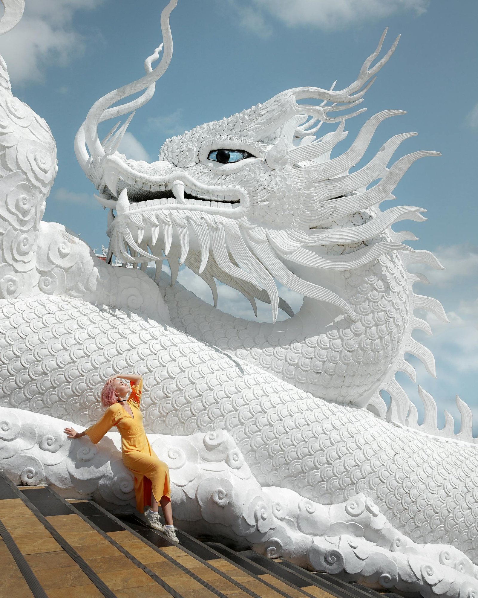 A woman in a yellow dress poses by the iconic dragon sculpture at Wat Huay Pla Kang, Thailand.