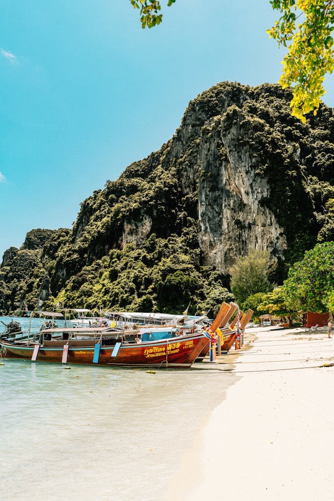 Colorful longtail boats docked on the sandy shores of Ko Panyi with limestone cliffs.