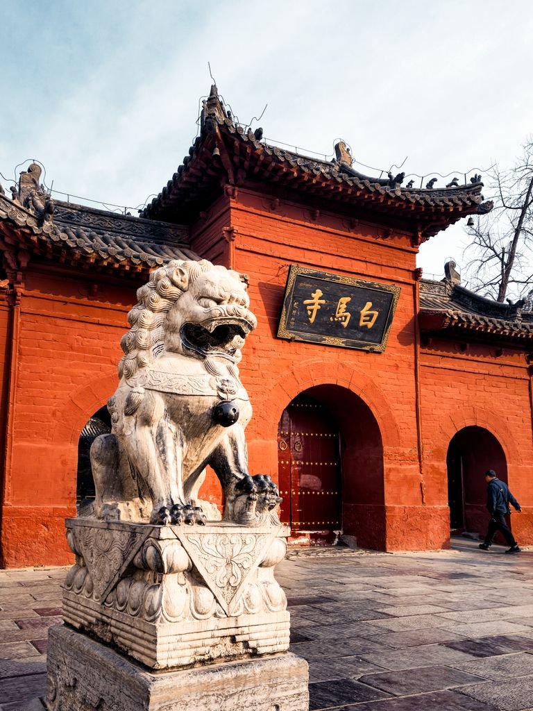 Historic Chinese temple entrance with a stone lion statue and red walls.