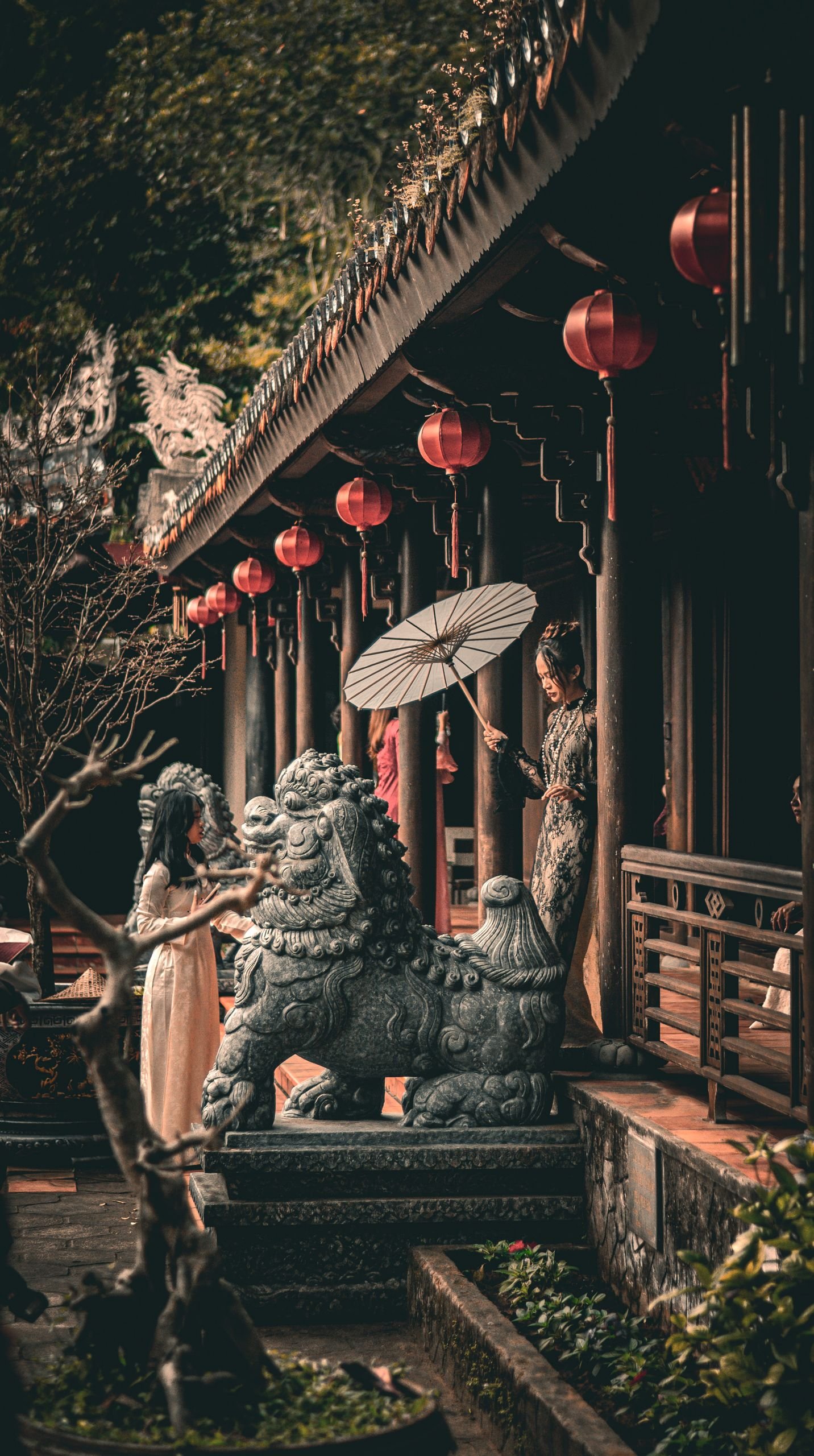 Scenic view of an Asian temple with a stone lion statue, lanterns, and traditional architecture.